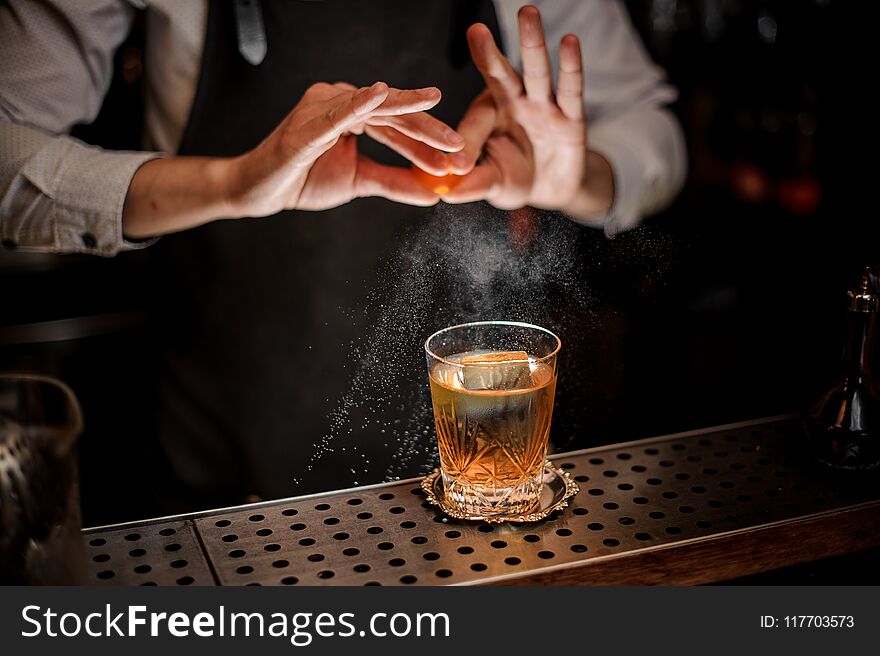 Professional bartender adding juice from the orange zest to the fresh alcoholic cocktail drink on the bar counter. Professional bartender adding juice from the orange zest to the fresh alcoholic cocktail drink on the bar counter