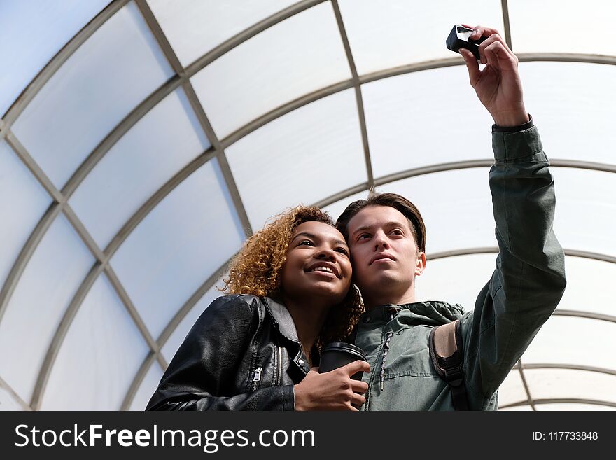 Cute international friends-students are photographed together ine a glass dome. A modern beautiful African American girl smiles when together with a white guy they make selfi on an action camera. Cute international friends-students are photographed together ine a glass dome. A modern beautiful African American girl smiles when together with a white guy they make selfi on an action camera.