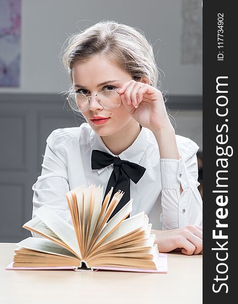 Charming successful businesswoman in glasses with a book at the table sits