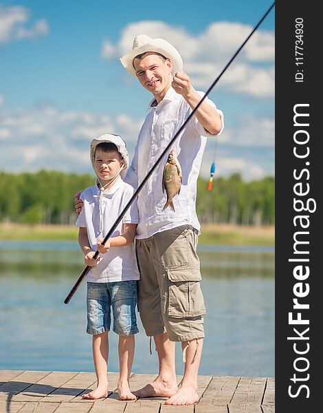 Vertical portrait of the father and son on the pier with a big fish on the hook, fishing on the lake