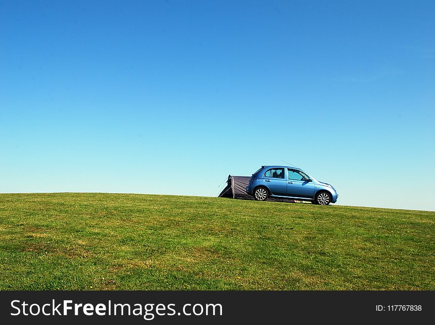 Blue Hatchback On Green Grass Field Under Blue Sky