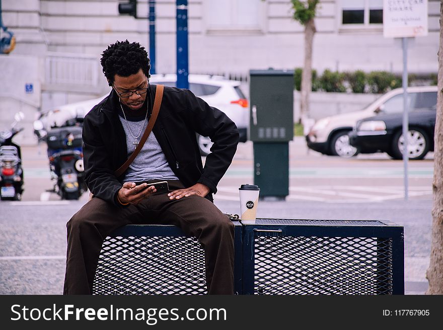 Man Wearing Black Bomber Jacket And Holding Smartphone