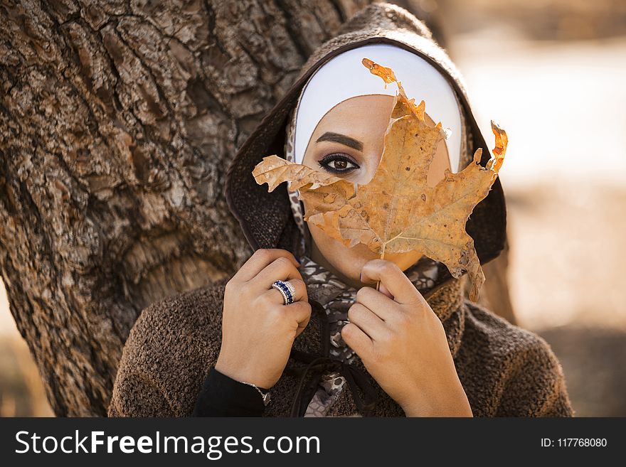 Woman Leaning On Brown Tree Holding Brown Leaf Covering Her Face