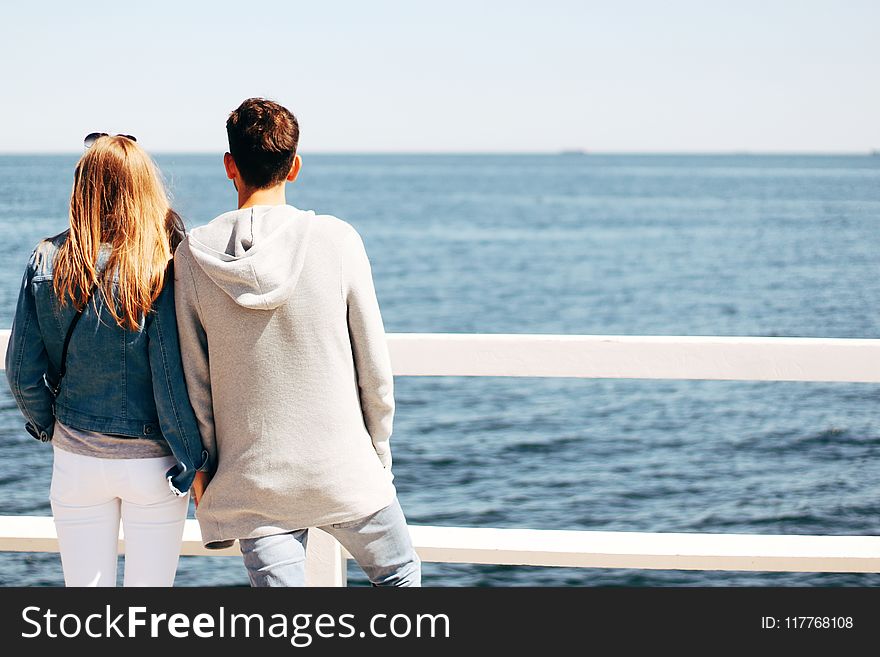 Man and Woman Beside Wooden Hand Rail Beside Body of Water