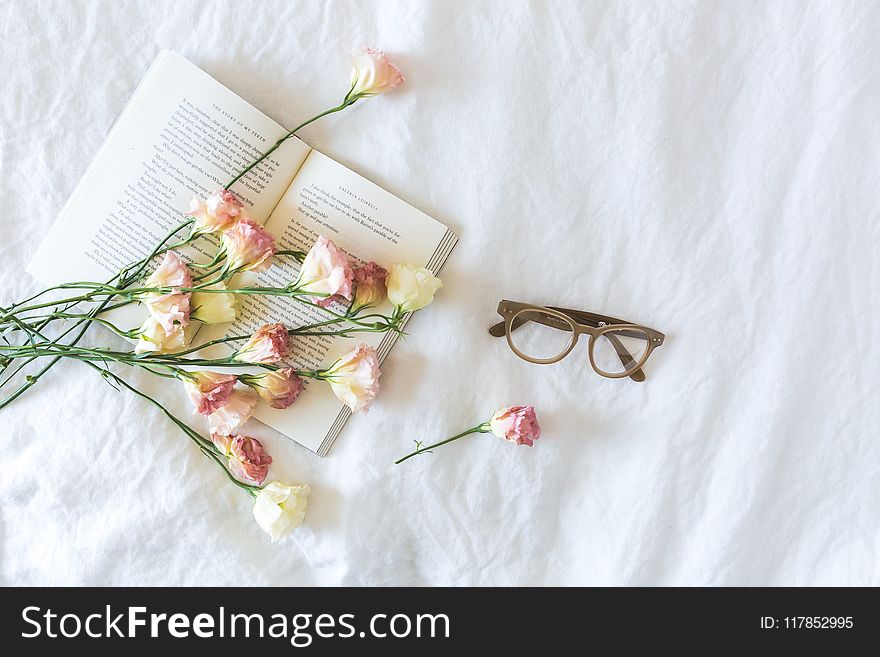 White and Pink Flowerson a book beside Eyeglasses