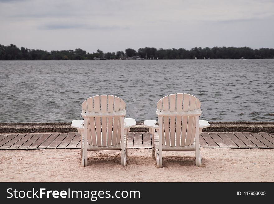Two White Lounge Chairs Beside Body of Water