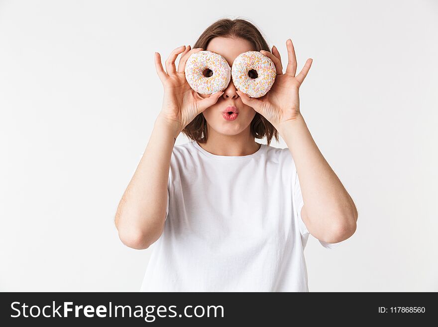 Portrait of a smiling young woman holding two donuts at her face isolated over white background