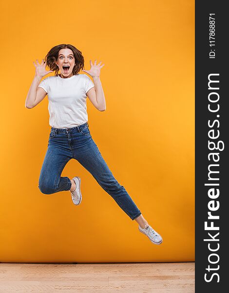 Photo of emotional young woman jumping isolated over yellow background. Looking camera.