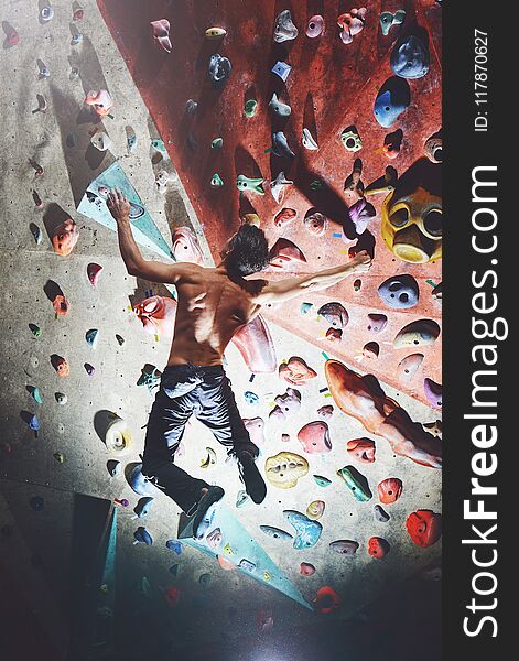 A man climber climbs indoors in bouldering gym. Athletic man climbing up on practice wall
