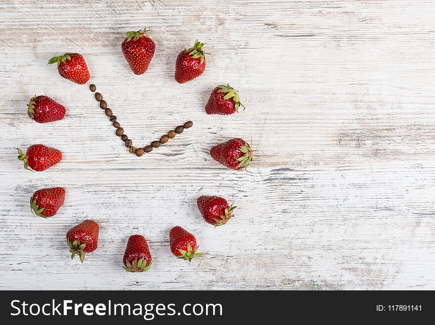 strawberry clock with arrows from coffee beans showing the time thirteen hours fifty-five minutes or one hour fifty-five minutes on a wooden old background in the kitchen. Flat Lay. Background for a postcard, banner, site, advertisement