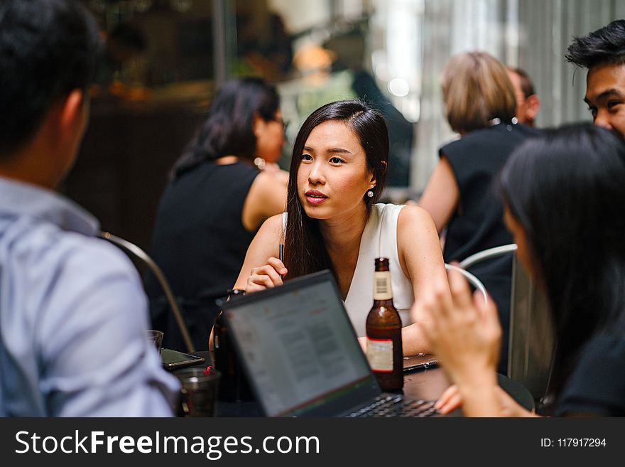 Woman Wearing White Top Sitting Near Table With People