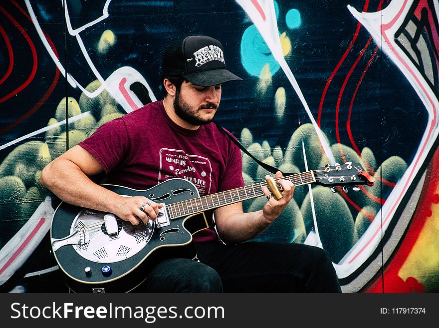 Man in Red Shirt Playing Resonator Guitar Near Wall With Black and Green Painting