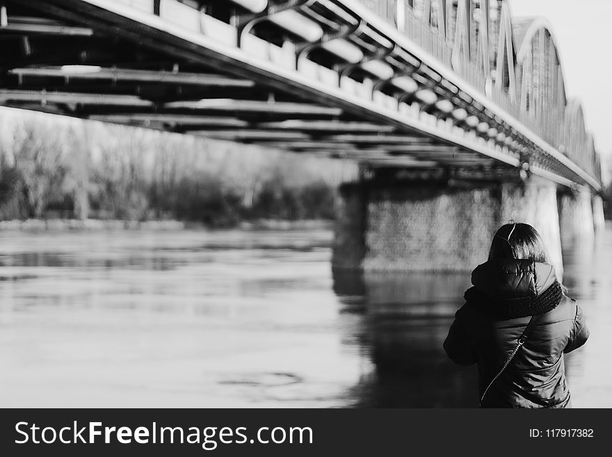 Grayscale Photo Of Person Wearing Jacket Near Bridge