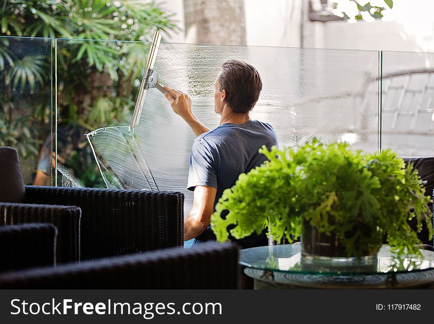 Man In Gray Shirt Cleaning Clear Glass Wall Near Sofa