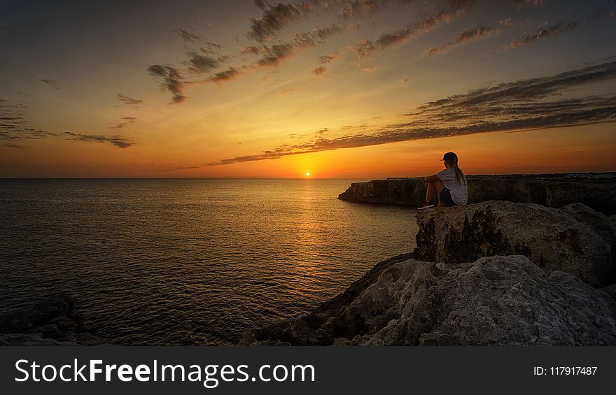 Photo of Person Sitting on Rock During Sunset