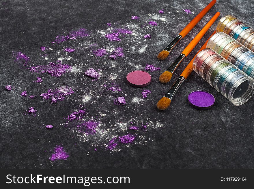 Collection of brushes with palette near pink and purple loose eye shadows lying on a black background. concept of professional cosmetics. free space for text. Collection of brushes with palette near pink and purple loose eye shadows lying on a black background. concept of professional cosmetics. free space for text