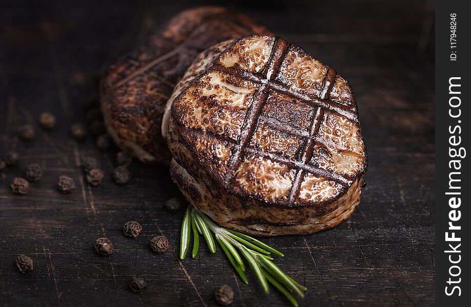 Grilled juicy beef pork steak slice on wooden background with pepper and rosemarine herb