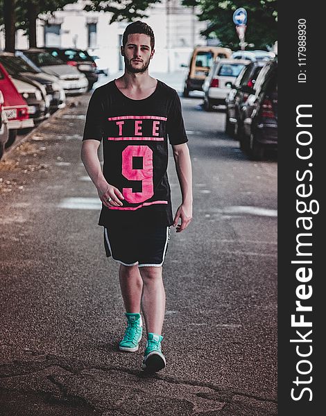 Man Wearing Black Crew-neck T-shirt, Black Shorts, and Pair of Teal High-top Sneakers Walking Between Vehicles
