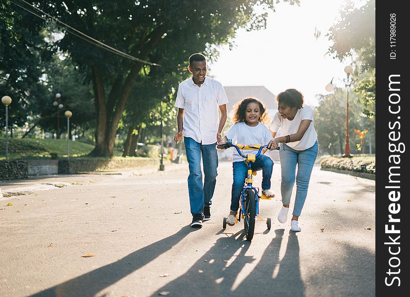Man Standing Beside His Wife Teaching Their Child How to Ride Bicycle