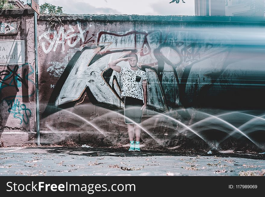 Man In White Shirt And Black Shorts Saluting Graffiti At Daytime