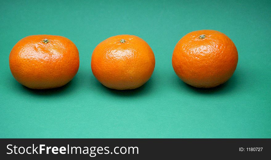 Three orange tangerines in a row on a contrasting and colourful green background. Three orange tangerines in a row on a contrasting and colourful green background.
