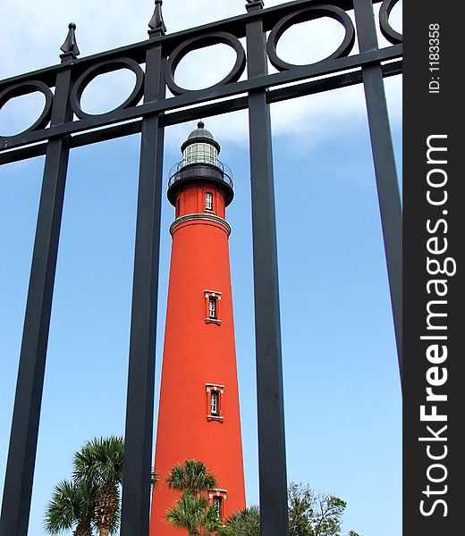 Red brick lighthouse in Ponce Inlet Florida framed by wrought iron fence. Red brick lighthouse in Ponce Inlet Florida framed by wrought iron fence.