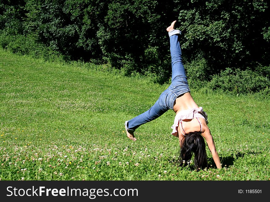 A young woman makes a handstand on grass in front of blue sky