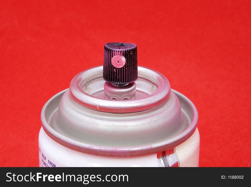 The nozzle portion of a can of pink spray paint. On a red background. The nozzle portion of a can of pink spray paint. On a red background.