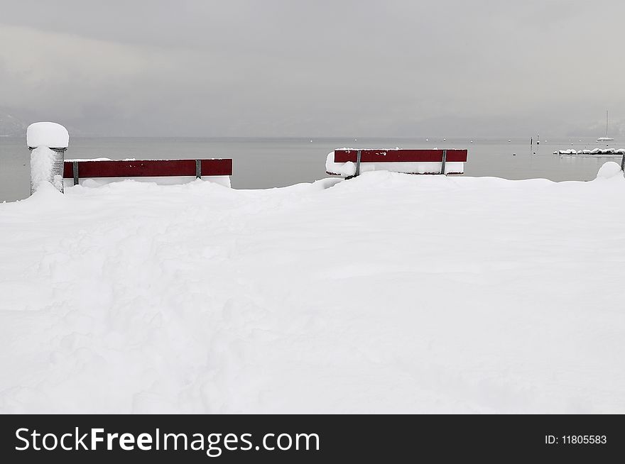 Red colored and deeply snow covered benches in front of Lake Thun. Red colored and deeply snow covered benches in front of Lake Thun