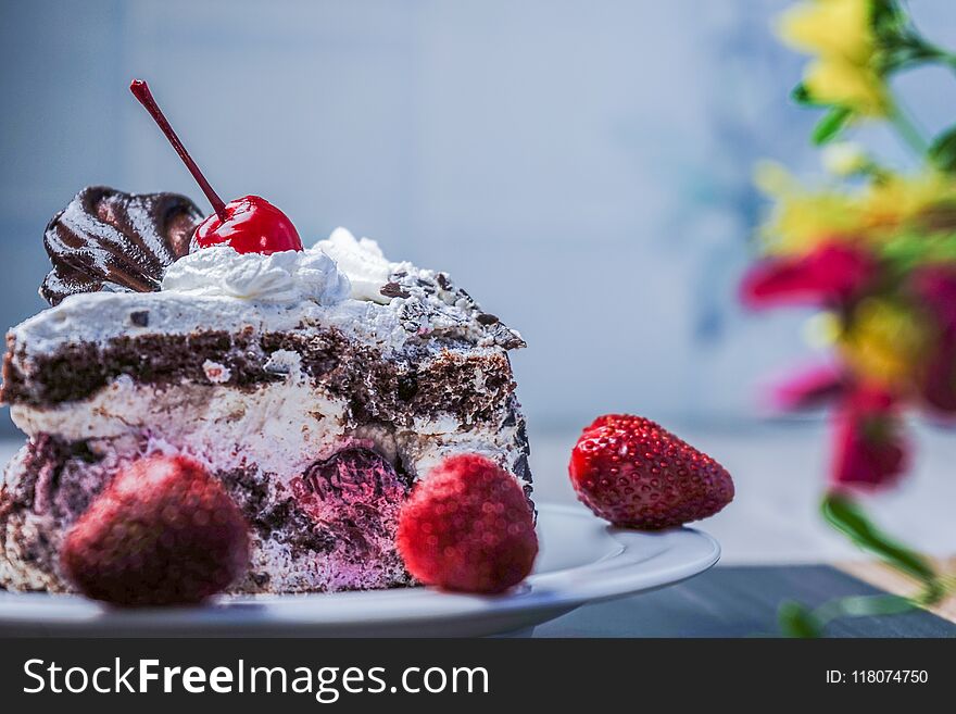 Slice of cake with cherries and strawberries on a table with flowers