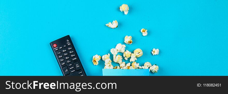 Box of popcorn spilled on blue background.