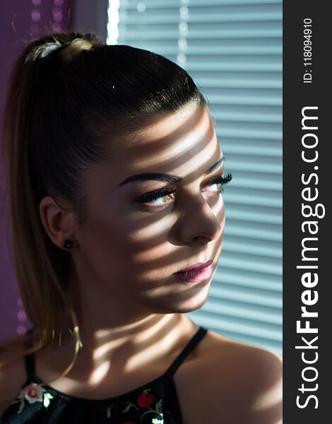 Serious Girl Face With Shadow Of Venetian Blinds Looking Through Window In Sunset At Home