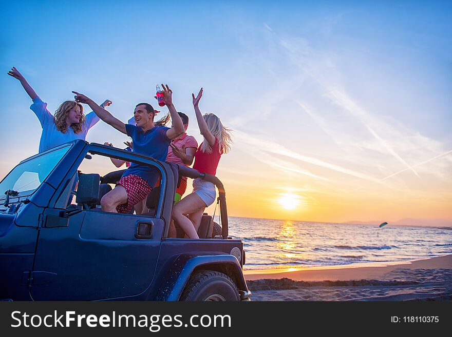 Young people having fun in convertible car at the beach at sunset.