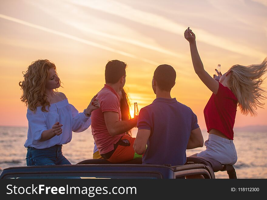 Five young people having fun in convertible car at the beach at