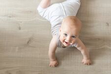 Cute Little Baby Boy Lying On Hardwood And Smiling. Child Crawling Over Wooden Parquet And Looking Up With Happy Face. View From A Royalty Free Stock Image