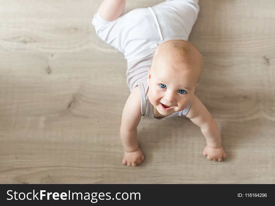 Cute little baby boy lying on hardwood and smiling. Child crawling over wooden parquet and looking up with happy face. View from a