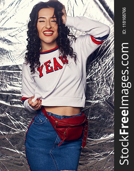 Young stylish crazy girl in blue jeans skirt and white hoodie standing and posing against silver background. Happy female having fun. Young stylish crazy girl in blue jeans skirt and white hoodie standing and posing against silver background. Happy female having fun