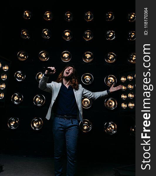 men singer with microphone on the stage, with long hair, against the background of bright lanterns, scene. men singer with microphone on the stage, with long hair, against the background of bright lanterns, scene