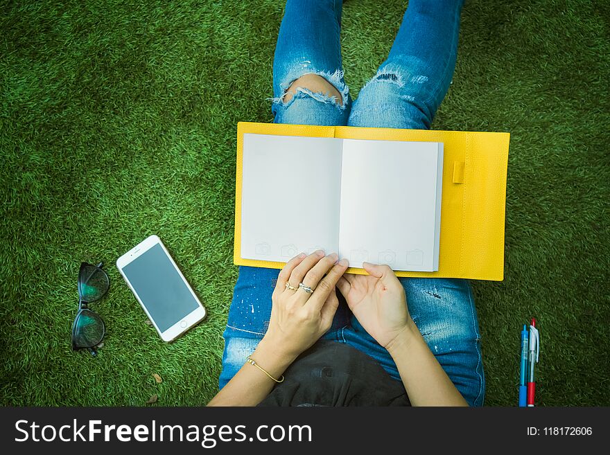 Girl,woman looking at the book and smartphone sitting in park.