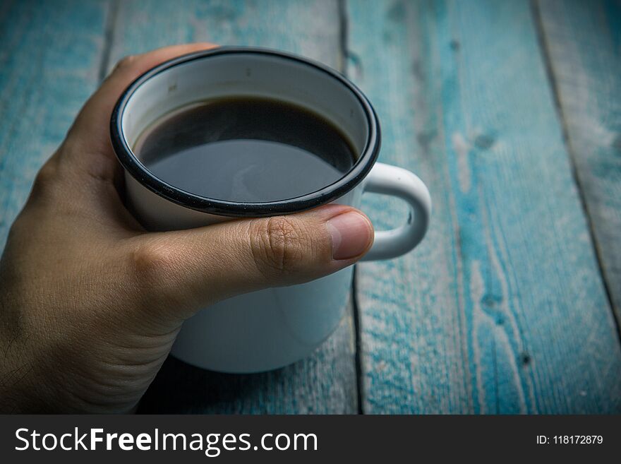 man holding in hand white iron mug with coffee or black tea on an old blue wooden table