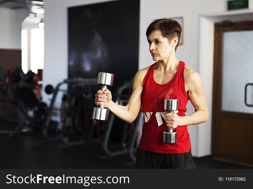 The woman in the gym doing exercises with dumbbells