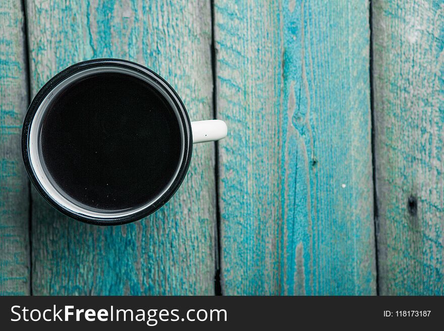 overhead view of a white iron mug with coffee or black tea on an old blue wooden table. overhead view of a white iron mug with coffee or black tea on an old blue wooden table