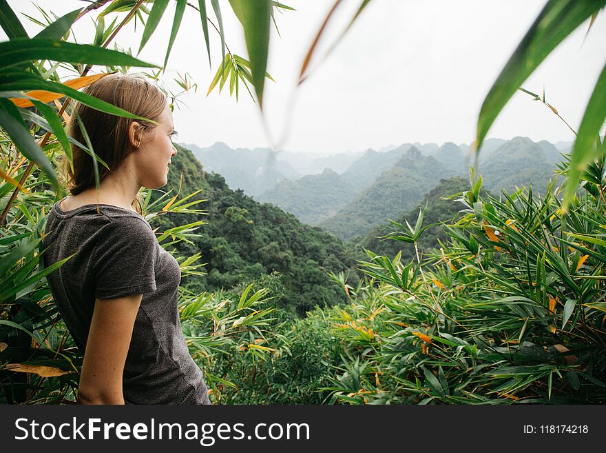 The concept of travel, tourism and people - a single woman is standing on top of a mountain among trees and looking on the panorama of mountains , Cat Ba, Vietnam. The concept of travel, tourism and people - a single woman is standing on top of a mountain among trees and looking on the panorama of mountains , Cat Ba, Vietnam