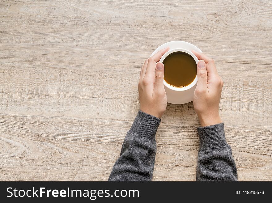 A cup of coffee in hand of women on wooden texture background.