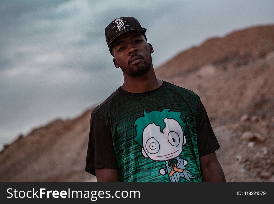 Man in Black and Green Crew-neck T-shirt Standing on Mountain Selective Focus Photography
