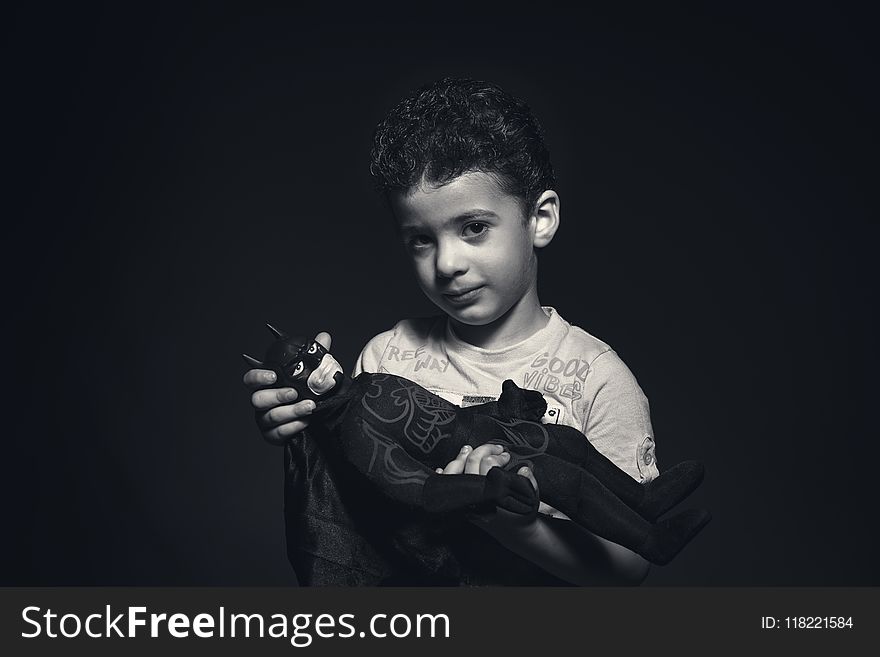 Grayscale Photo of a boy Holding Batman Plush Toy