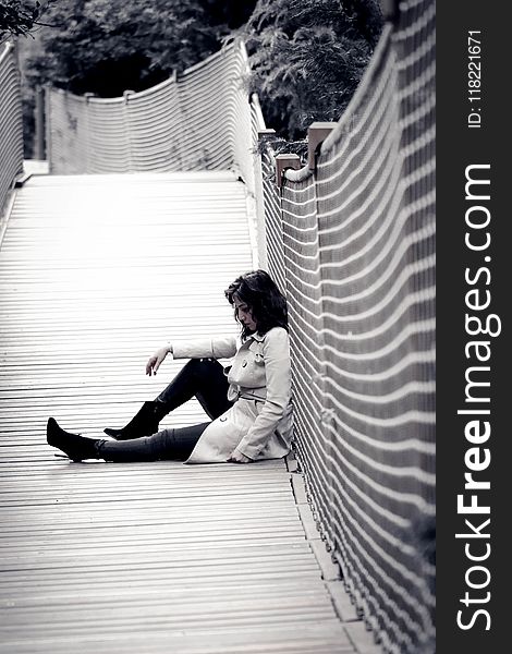 Low Light Photo of Woman Wearing Trench Coat Sitting Against Wall