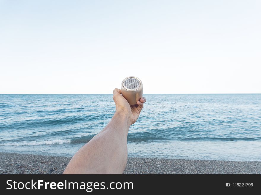 Person Holding Upward Brown Speaker in Front of Sea