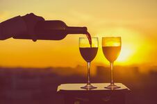 Female Hand With Bottle Pours Red Wine Into Glasses On A Sunset Background. Stock Photography