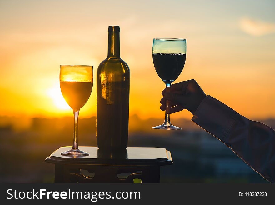 Silhouette of female hand toasting wine on sunset background.